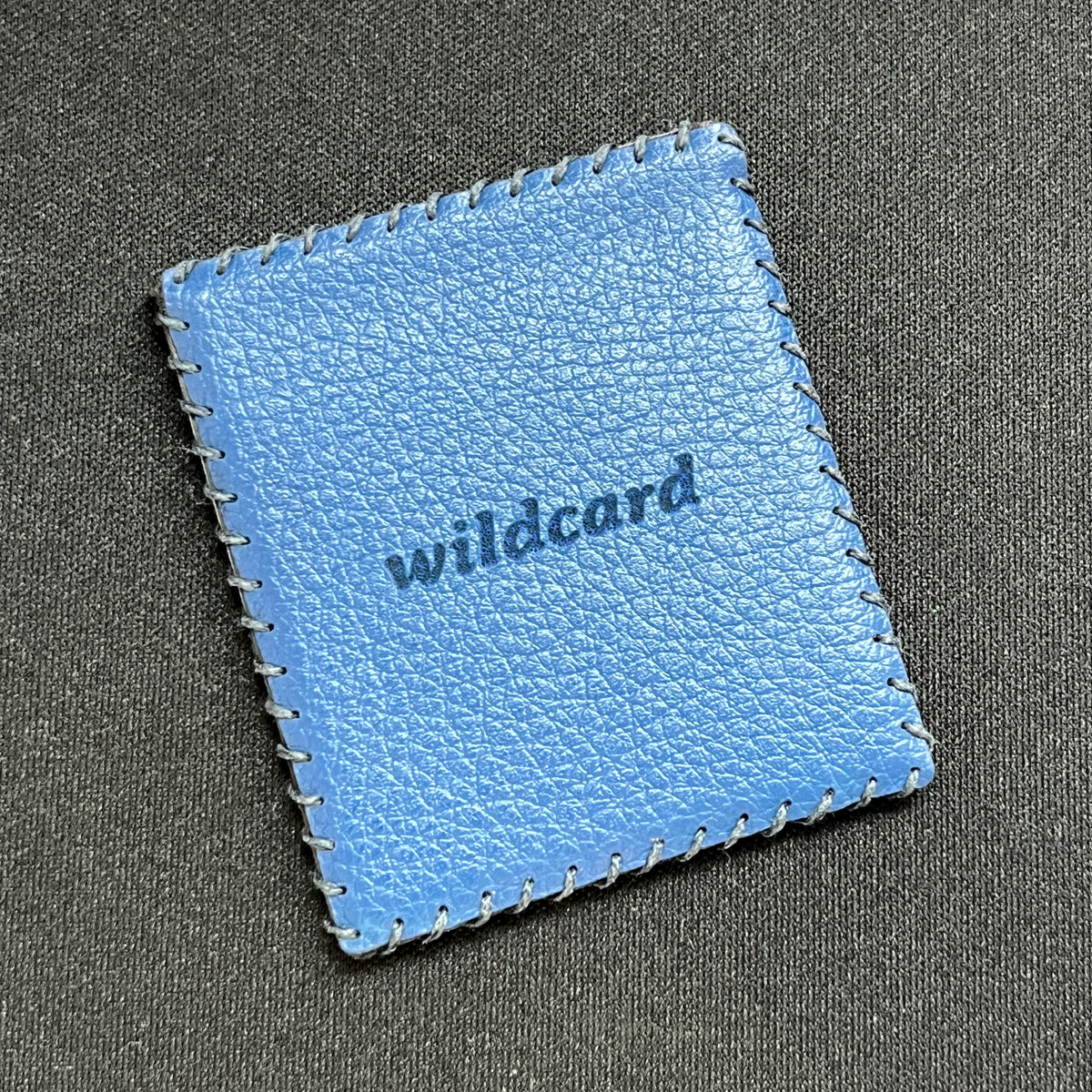 Wildcard Cobalt Cactus Classic, Small, held between two fingers to show its slim profile
